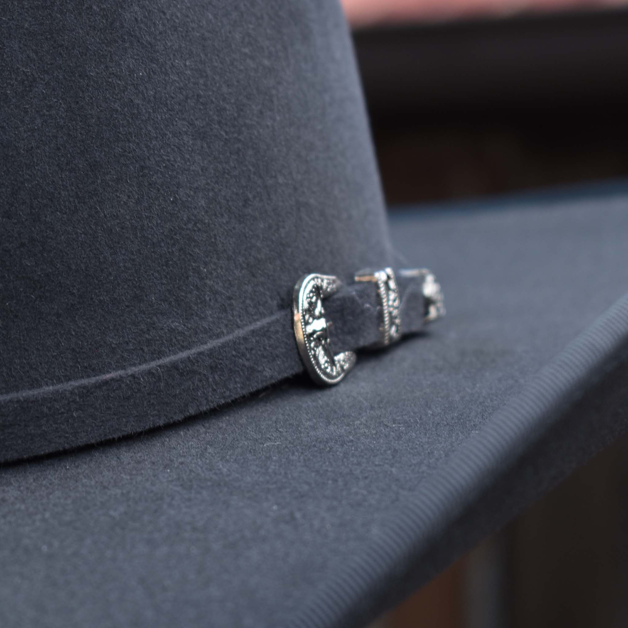 Close up photo of silver buckle featured on charcoal grey hat