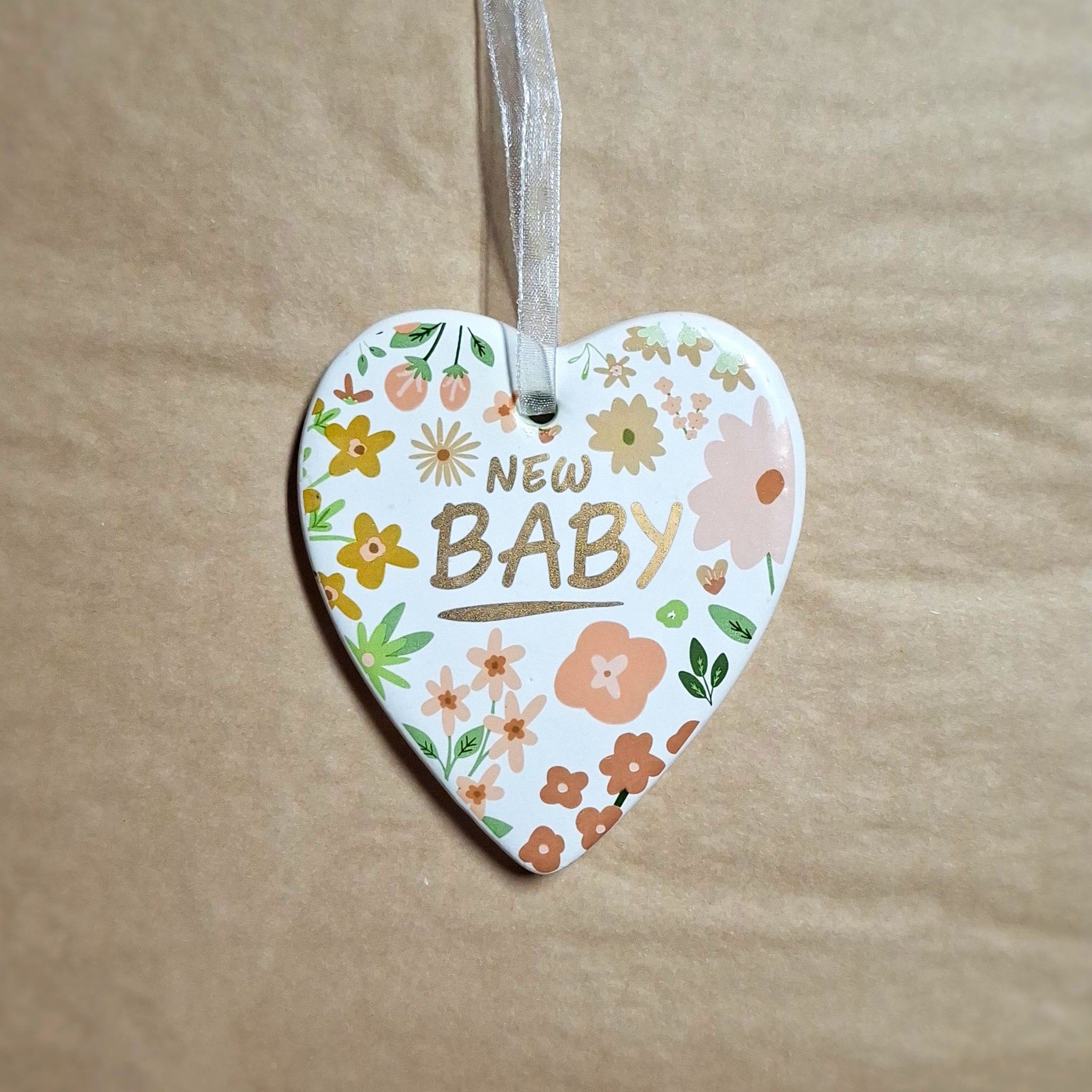 Ceramic heart with floral painting and gold writing saying New Baby, on a beige background