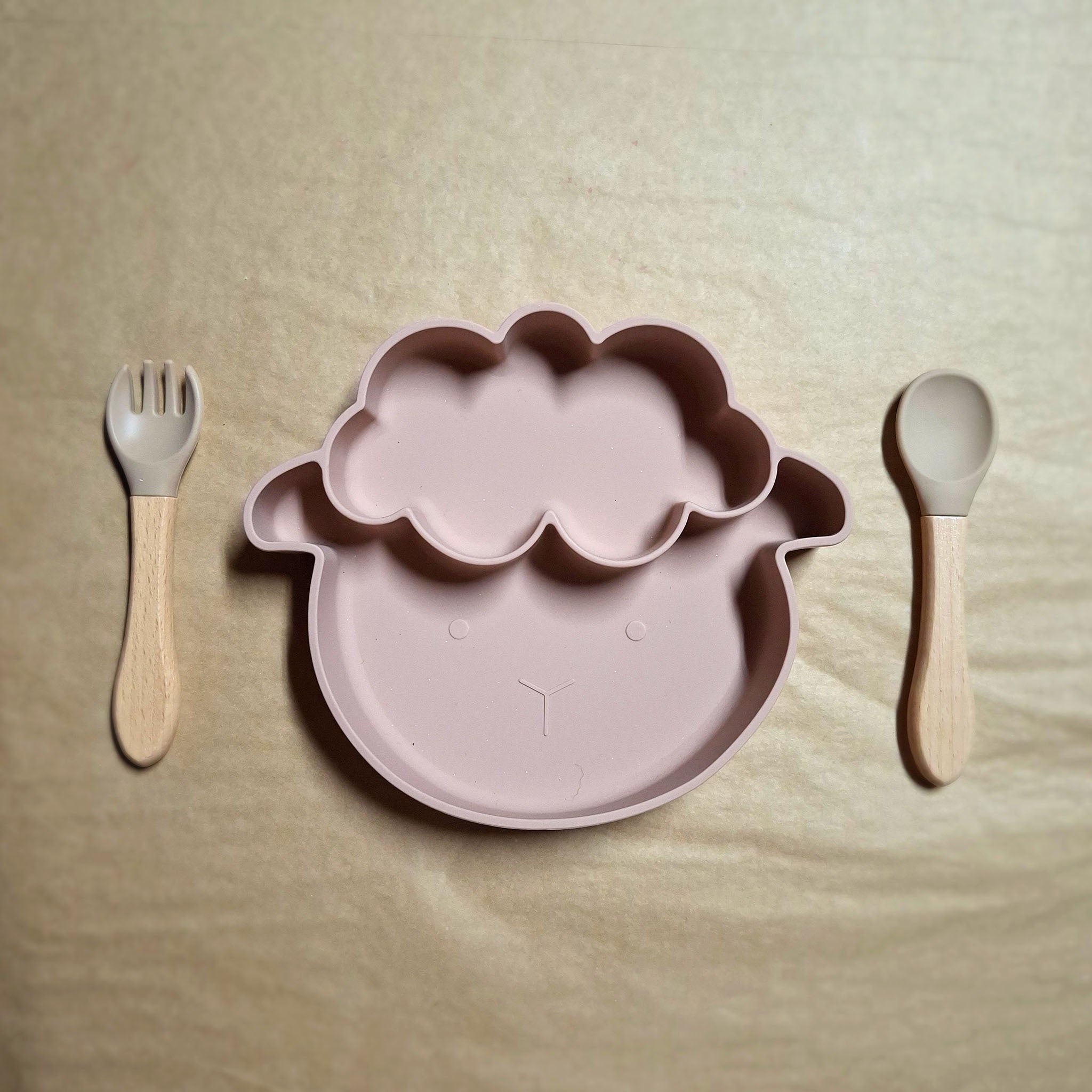 Silcone sheep shaped plate with silicone spoon and fork on beige backround