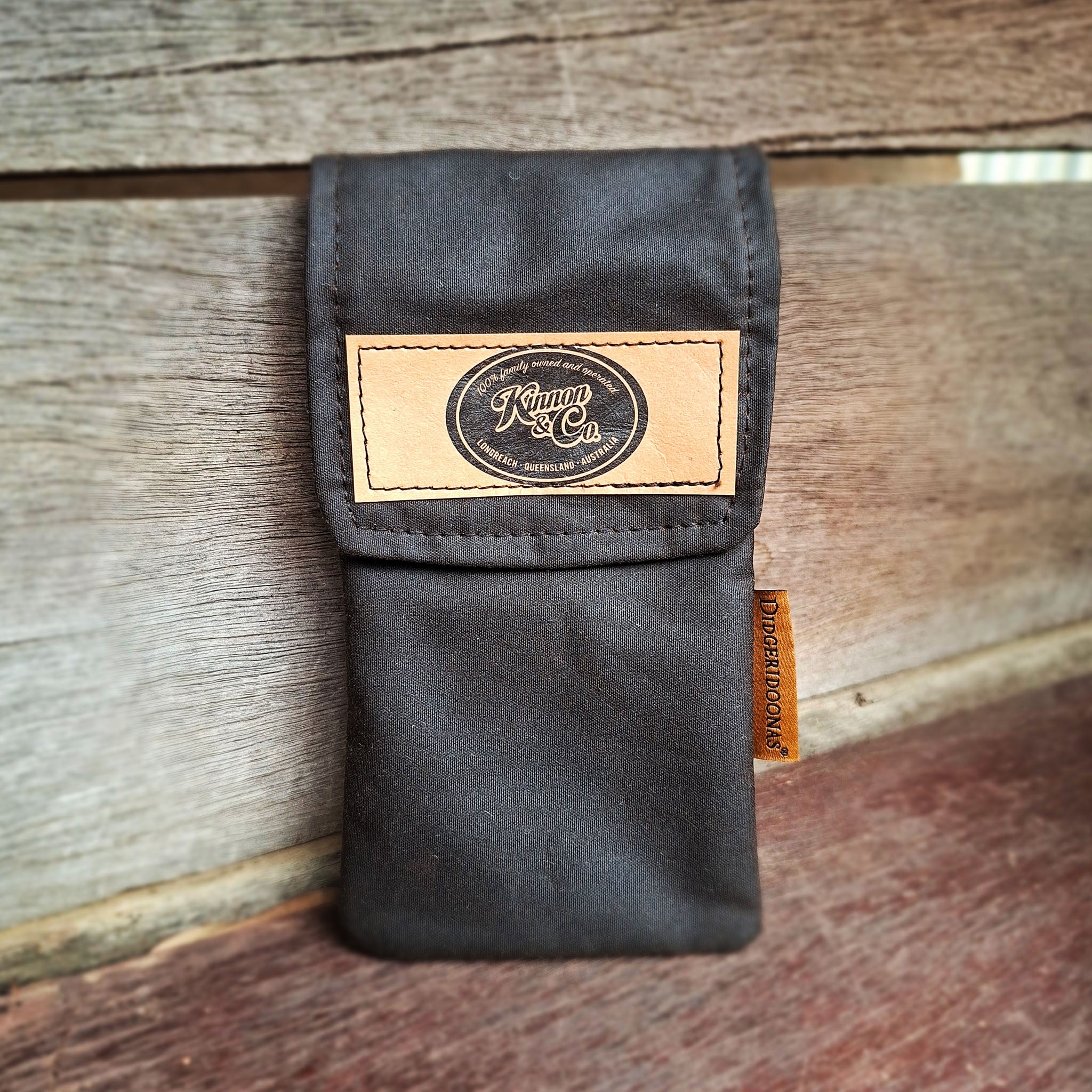 Black oilskin phone pouch featuring a tan leather label with Kinnon and Co branding