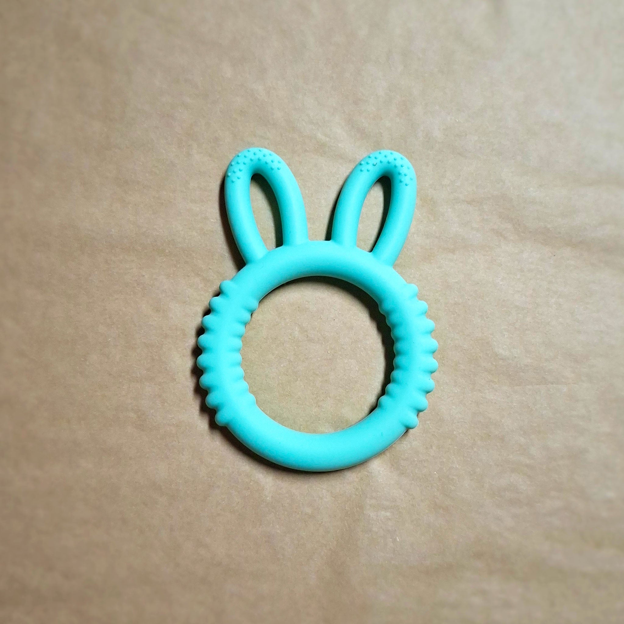 Bunny shaped silicone teether in aqua on beige background