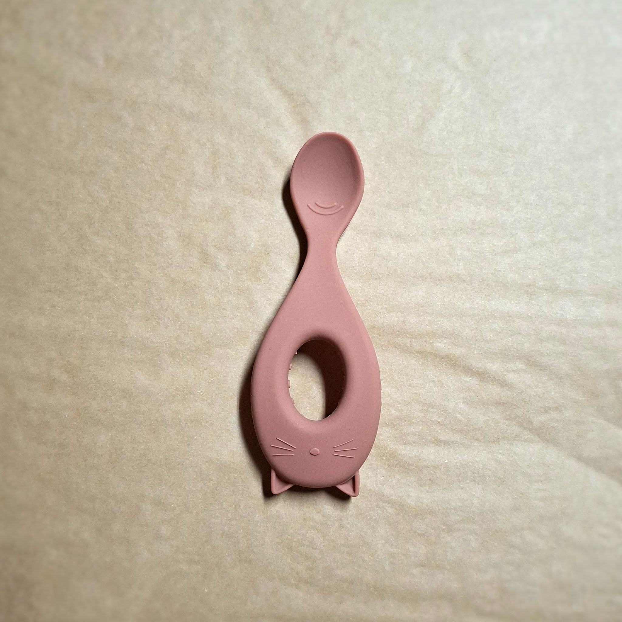 Dusty pink silicone feeding spoon on beige background